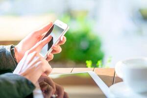 Person using smartphone while sitting at a table near a window with natural light in a relaxed setting photo