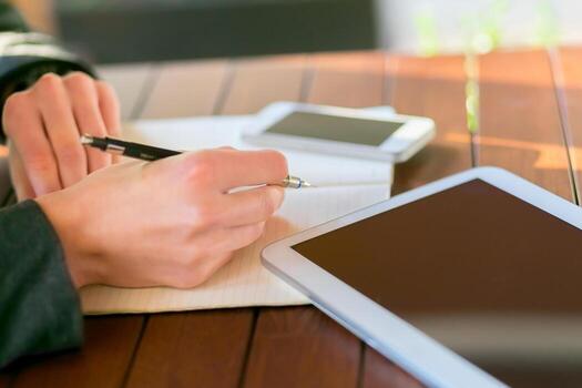 Writing notes and using devices at a wooden table in a bright, modern setting photo