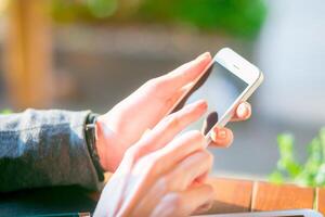 Person using smartphone outdoors in a sunny setting while sitting at a table photo
