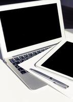 Technology setup with laptop, tablet, and pen on a white desk in a modern workspace for productivity and organization photo
