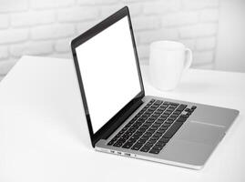 Laptop on a desk with a blank screen and a coffee mug in a minimalistic workspace photo
