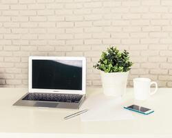 Workspace setup with laptop, smartphone, plant, and coffee on a clean table in a well-lit environment photo