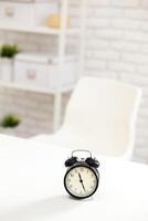 Clock placed on a table in a minimalistic workspace with a white chair and organized shelves photo