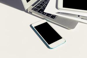 Smartphone placed next to laptop and tablet on a clean white desk during a productive work session photo