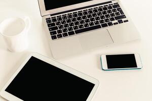 Tech devices arranged on a white table showcasing a laptop, tablet, and smartphone during a work session photo