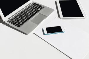 Modern workspace setup featuring laptop, tablet, smartphone, and blank paper on minimalist table photo