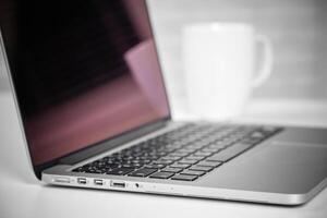 Laptop on table with cup of coffee in background creates a cozy workspace atmosphere photo