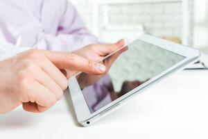 Person interacting with a tablet device while seated at a desk in a bright, modern workspace photo
