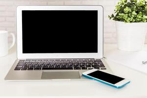 Workspace setup with a laptop and smartphone on a desk near a potted plant and a mug during daylight hours photo