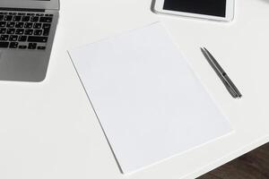 Blank paper on a workspace with a laptop and tablet during daylight showing a minimalist office setting photo