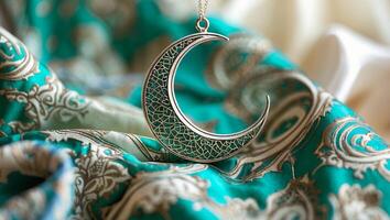 Elegant crescent moon pendant resting on ornate teal fabric with intricate patterns photo
