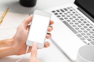 Engaging with a smartphone while sitting at a workspace with a laptop and stationery items photo