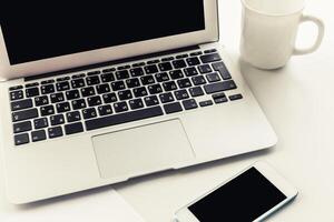 Workspace setup with laptop, smartphone, and coffee cup on a white desk during morning hours photo