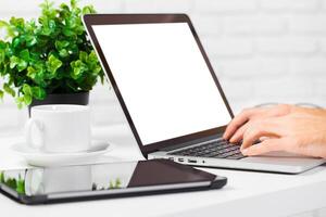 Working on a laptop with a cup of coffee and tablet on a desk surrounded by greenery photo