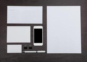 Collection of stationery items arranged on a wooden table including a smartphone and various paper formats photo