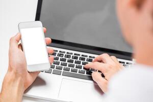 Person using smartphone while typing on laptop indoors in a modern workspace photo