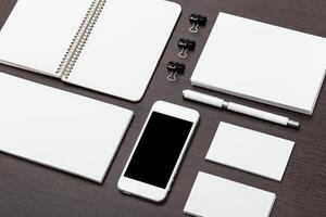 Collection of stationery items displayed on a wooden desk with a smartphone and various notepads at midday photo