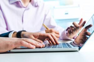 Group collaboration on a laptop in a modern office setting with focus on hands and technology photo
