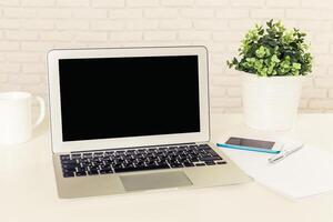Workspace setup with a laptop, notepad, and plant on a clean table in a bright environment photo