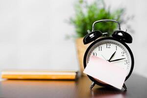 Clock on a desk with a note and a plant in the background during a quiet morning workspace photo