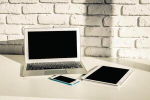 Modern workspace setup with laptop, smartphone, and tablet on minimalistic white table photo