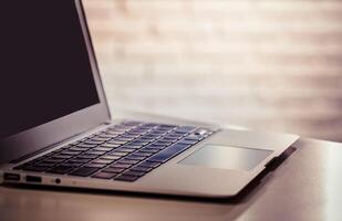 Laptop resting on a wooden table with a soft textured background in a well-lit space photo