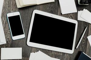 Desk workspace with tablet, smartphone, notebooks, blank cards, and pen in a quiet home office setting photo
