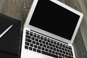 Laptop on a wooden table beside a notebook and pen during a work session in a cozy office setting photo