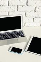 Workspace setup with laptop, tablet, and smartphone on a white brick background for productivity and creativity photo