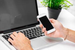 Person multitasking with a laptop and smartphone in a modern workspace during the day photo