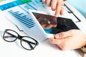 Professional analyzing data on tablet while reviewing charts and graphs in modern workspace photo