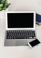 Workspace with a laptop and smartphone placed on a table beside a plant and notebook in a bright setting photo