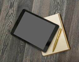 Digital tablet rests on a notepad with a pen on a wooden surface during a quiet study session in a cozy workspace photo
