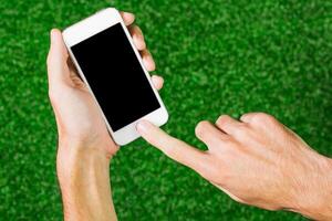 Person using smartphone on green grass surface during sunny day while engaging with digital content or application photo