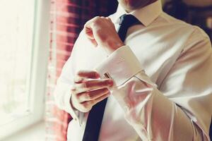 Man adjusting cufflinks while getting ready in elegant setting near window photo