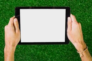 Hands holding a tablet on green grass with a blank screen ready for content creation or presentation photo