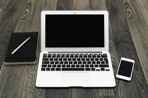 Workspace setup featuring a laptop, smartphone, notebook, and pen on a wooden desk during daylight hours photo