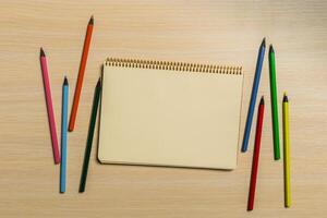 Colorful pencils surround a blank sketchpad on a wooden table inviting creativity and artistic expression photo
