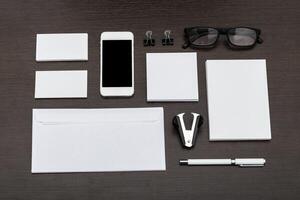 Office workspace setup with stationery and smartphone laid out on a dark wooden table at midday photo