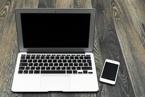 Modern laptop and smartphone placed on a wooden desk during a work-from-home session in bright lighting hours photo