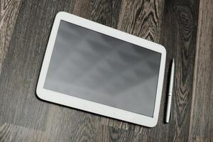 Tablet and pen resting on wooden surface in a modern workspace during daylight hours photo