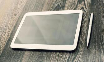 Digital tablet placed on wooden table with a pen nearby, showcasing workspace essentials for productivity photo