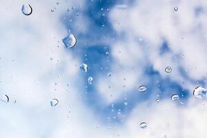 Raindrops cling to a window with a backdrop of blue sky and clouds in a serene afternoon photo