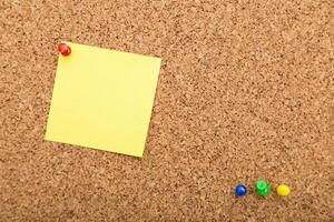 Yellow sticky note on corkboard with colored push pins arranged for task reminders or planning photo