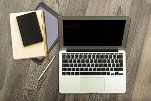 Workspace setup with laptop, notebook, and tablet on wooden table during the day photo