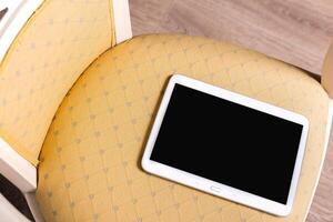 Tablet rests on patterned chair cushion in a cozy indoor setting during daylight hours photo