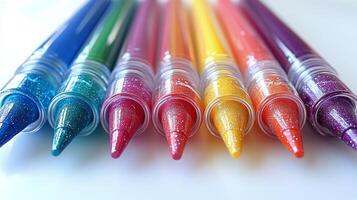 A row of colorful glitter pens on a white surface photo