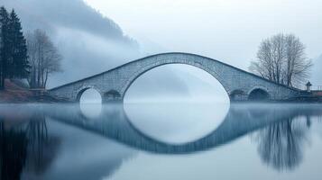 Serene stone bridge shrouded in morning mist reflecting in quiet waters of tranquil park photo