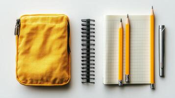 A yellow pencil case, a notebook, and two pencils are on a white surface photo
