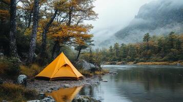 A yellow tent is set up on the shore of a river photo